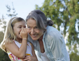 A young girl whispers into the ear of a smiling older woman
